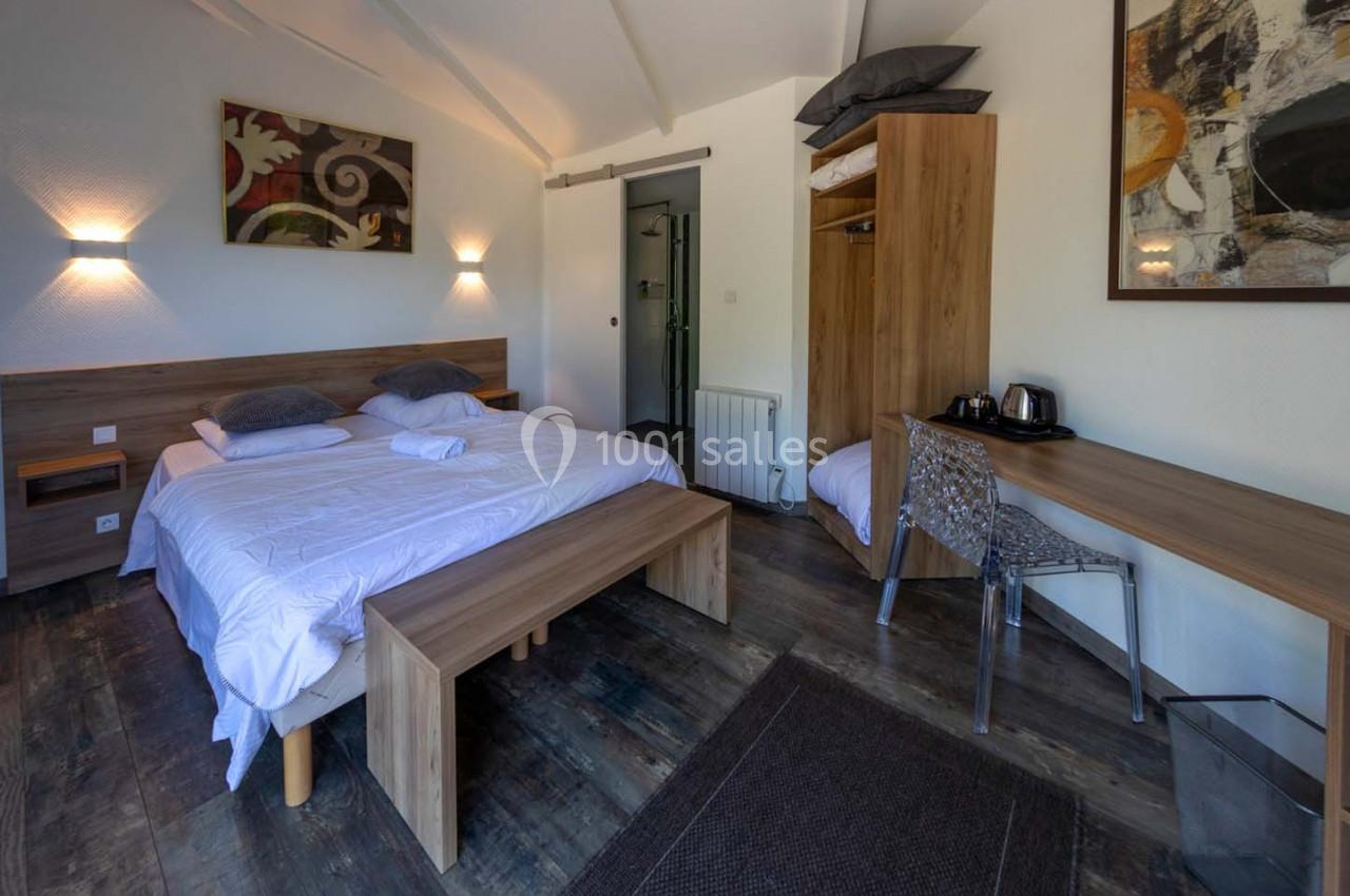 Location salle Saint-Aignan-de-Cramesnil (Calvados) - La Jalousie #23 Chambre lumineuse avec lit double, bureau, chaise transparente, armoire ouverte et décoration murale abstraite.