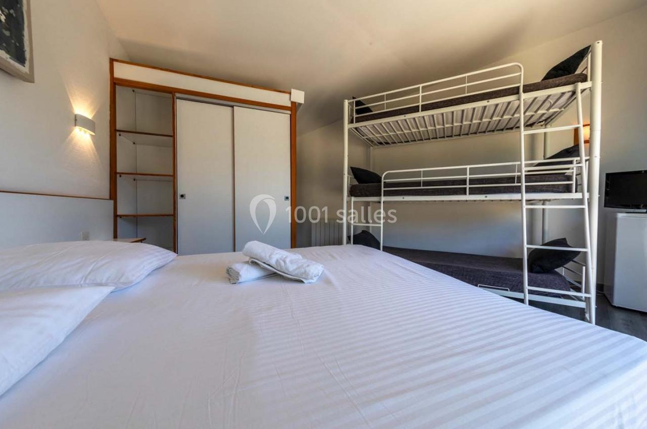 Location salle Saint-Aignan-de-Cramesnil (Calvados) - La Jalousie #24 Chambre avec un lit double, des lits superposés, une armoire, un mini-réfrigérateur et des serviettes pliées sur le lit.