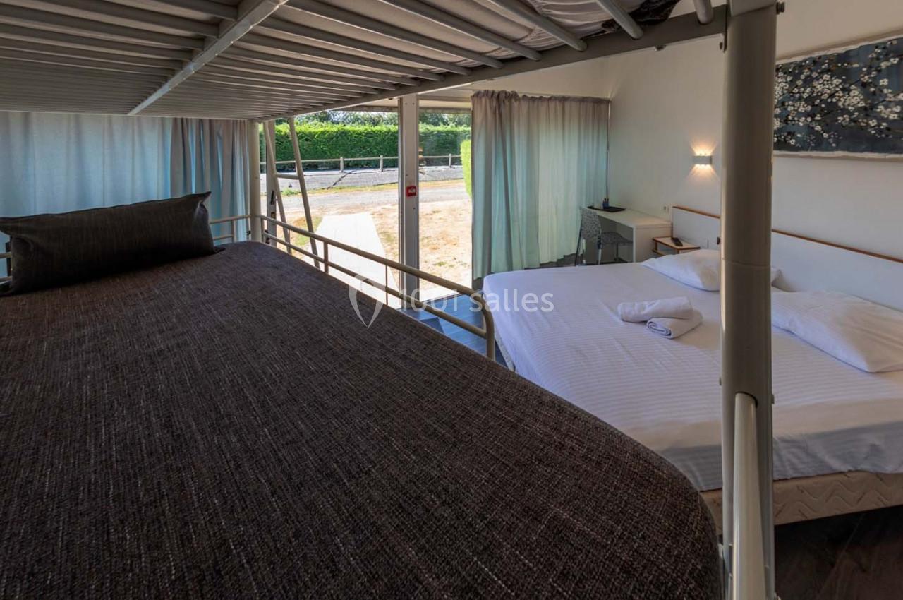 Location salle Saint-Aignan-de-Cramesnil (Calvados) - La Jalousie #25 Lit superposé et lit double dans une chambre lumineuse avec vue sur l'extérieur, rideaux ouverts et décoration murale.