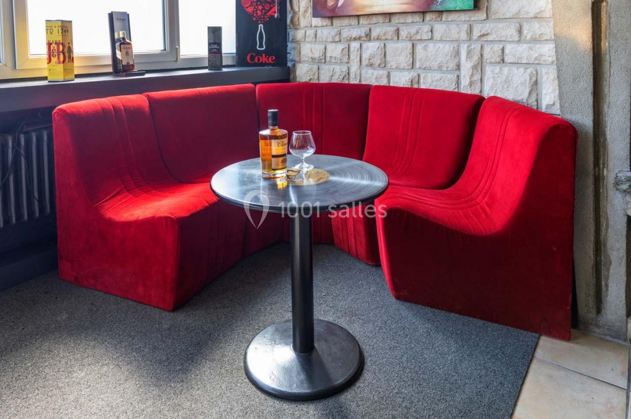 Location salle Saint-Aignan-de-Cramesnil (Calvados) - La Jalousie #5 Banquette rouge en arc de cercle autour d'une table ronde avec une bouteille de whisky et un verre posé dessus.