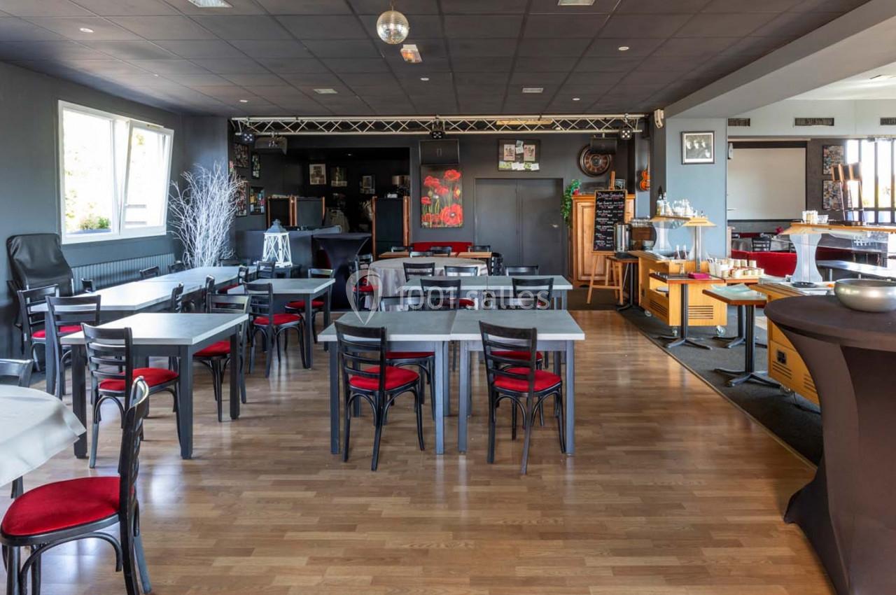 Location salle Saint-Aignan-de-Cramesnil (Calvados) - La Jalousie #3 Salle de restaurant lumineuse avec tables et chaises noires, parquet en bois clair et buffet en arrière-plan.