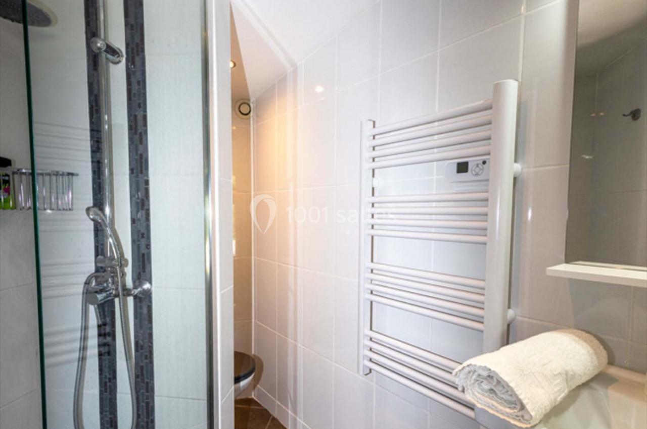 Location salle Saint-Aignan-de-Cramesnil (Calvados) - La Jalousie #26 Salle de bain moderne avec douche, sèche-serviettes mural, carrelage blanc et serviette pliée sur une étagère.
