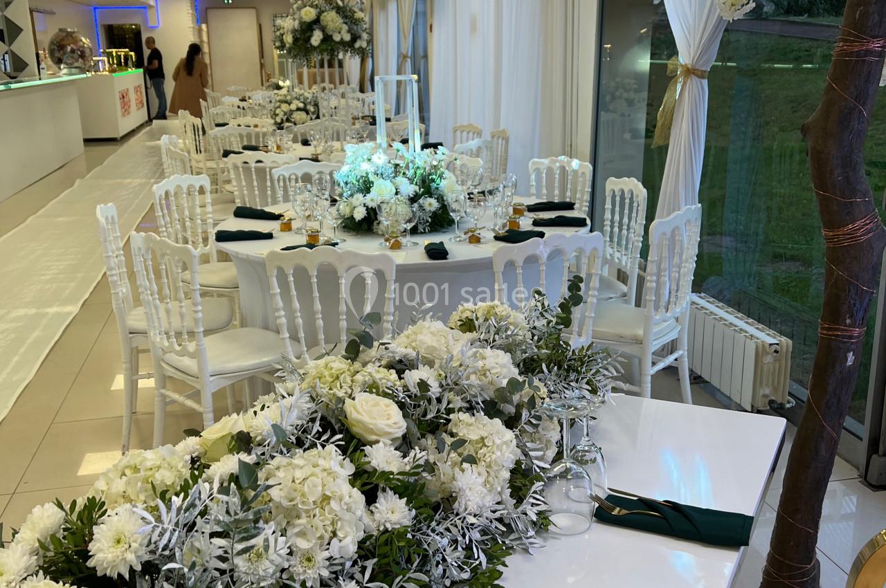 Salle de réception décorée avec des tables dressées, des fleurs blanches et une ambiance lumineuse élégante.