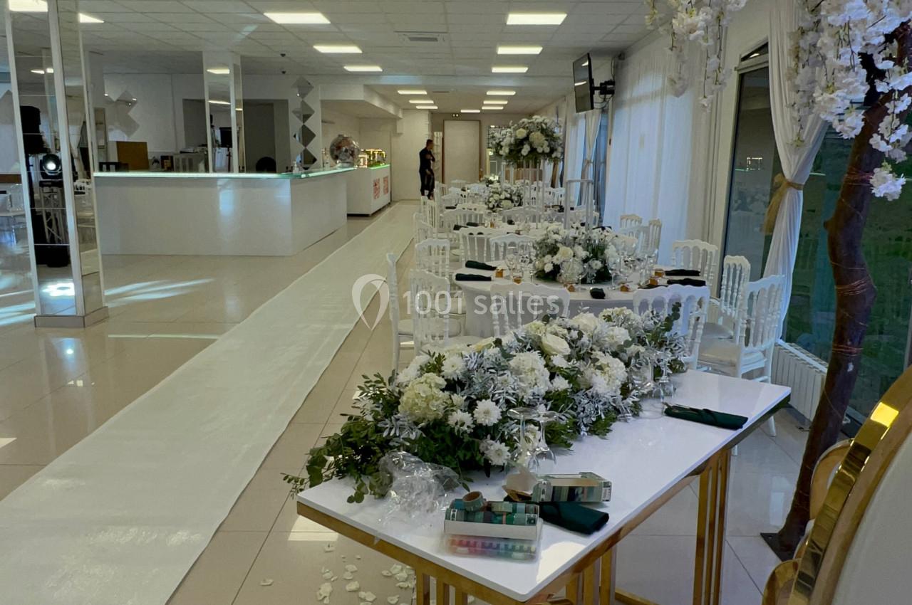 Salle de réception décorée pour un mariage, avec des tables ornées de fleurs blanches et une allée centrale.