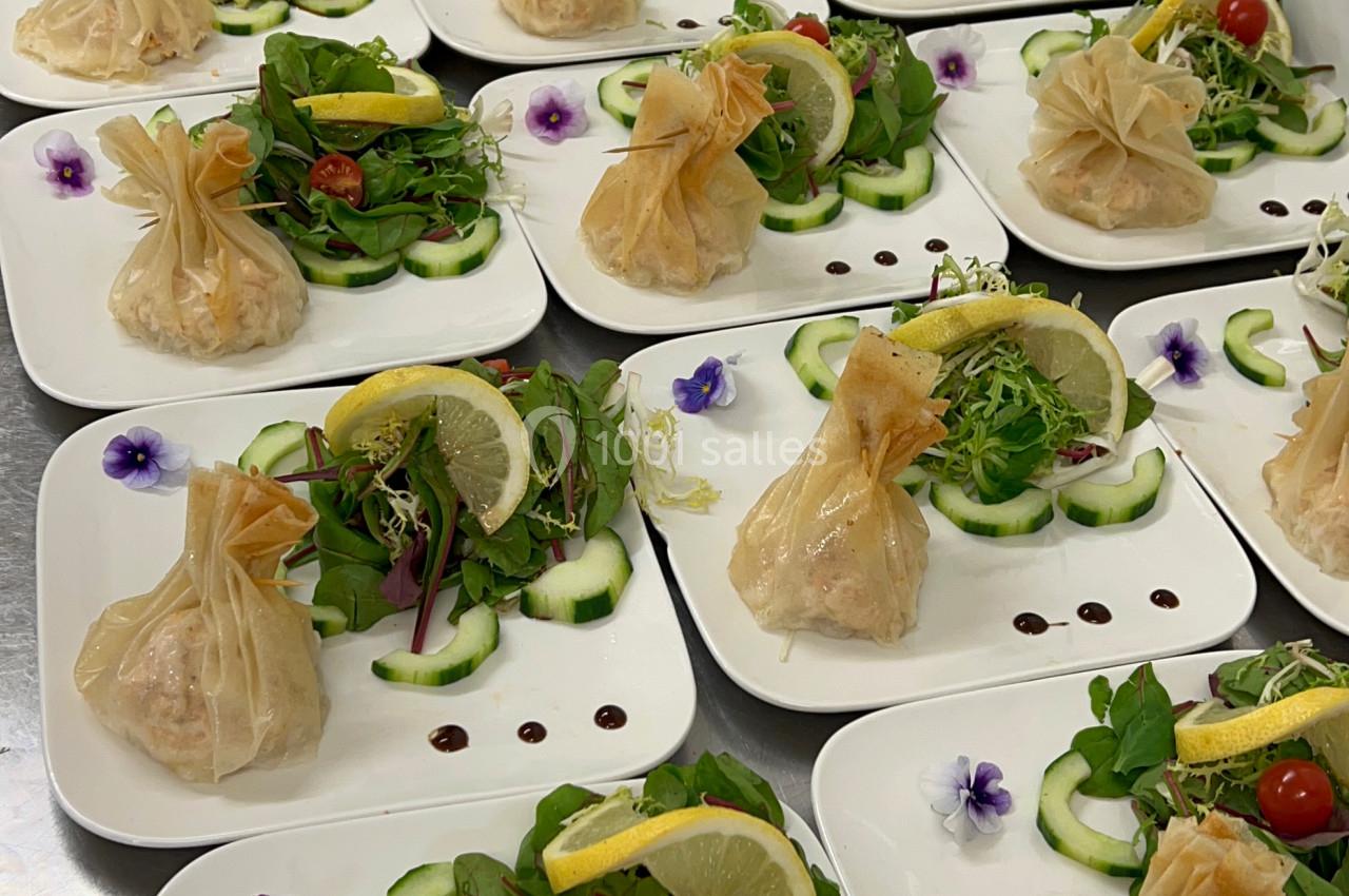 Assiettes dressées avec des aumônières dorées, salade verte, rondelles de concombre, tomates cerises et décorations florales.