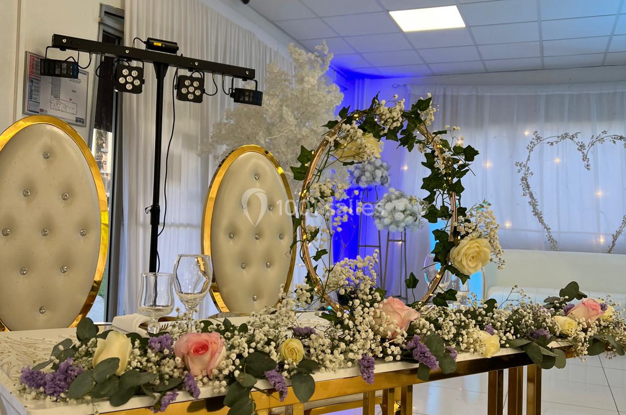 Table de mariage décorée avec des fleurs blanches et colorées, deux chaises élégantes et un éclairage en arrière-plan.