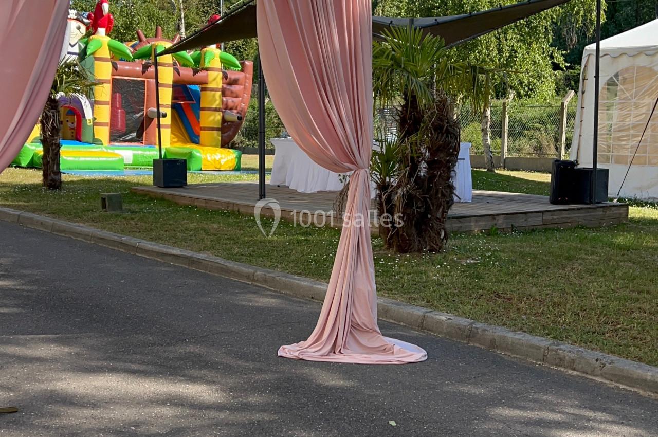 Rideaux roses encadrant une allée extérieure avec structures gonflables et tentes blanches en arrière-plan.