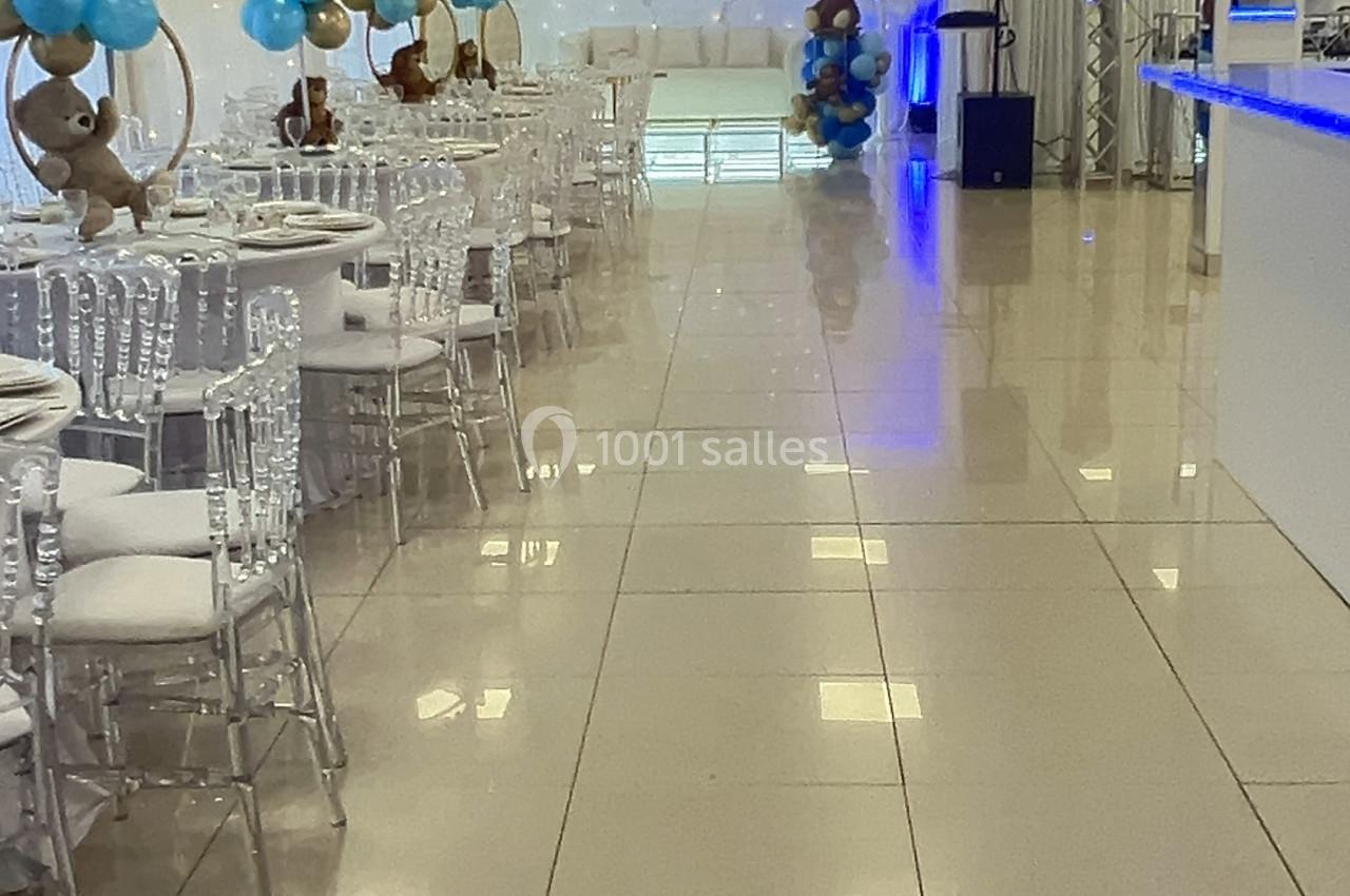 Salle de réception décorée avec des ballons bleus et dorés, tables dressées et éclairage tamisé.