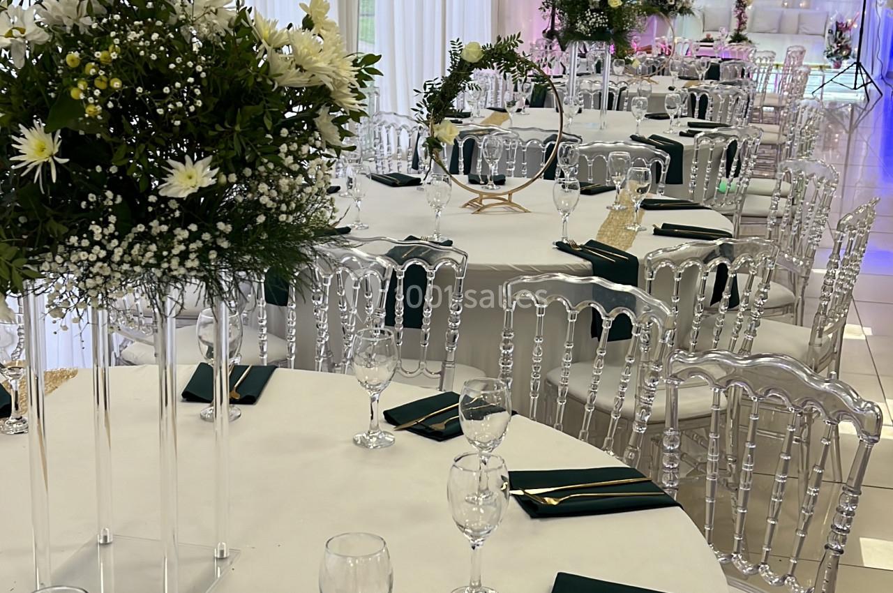 Salle de réception décorée avec des tables rondes, nappes blanches, serviettes vertes et centres de table fleuris.