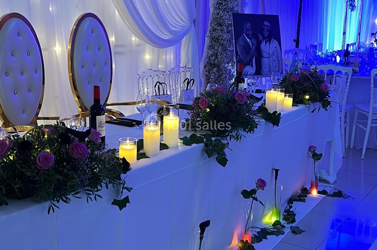 Table décorée pour un événement avec bougies LED, fleurs, chaises élégantes et éclairage bleu en arrière-plan.