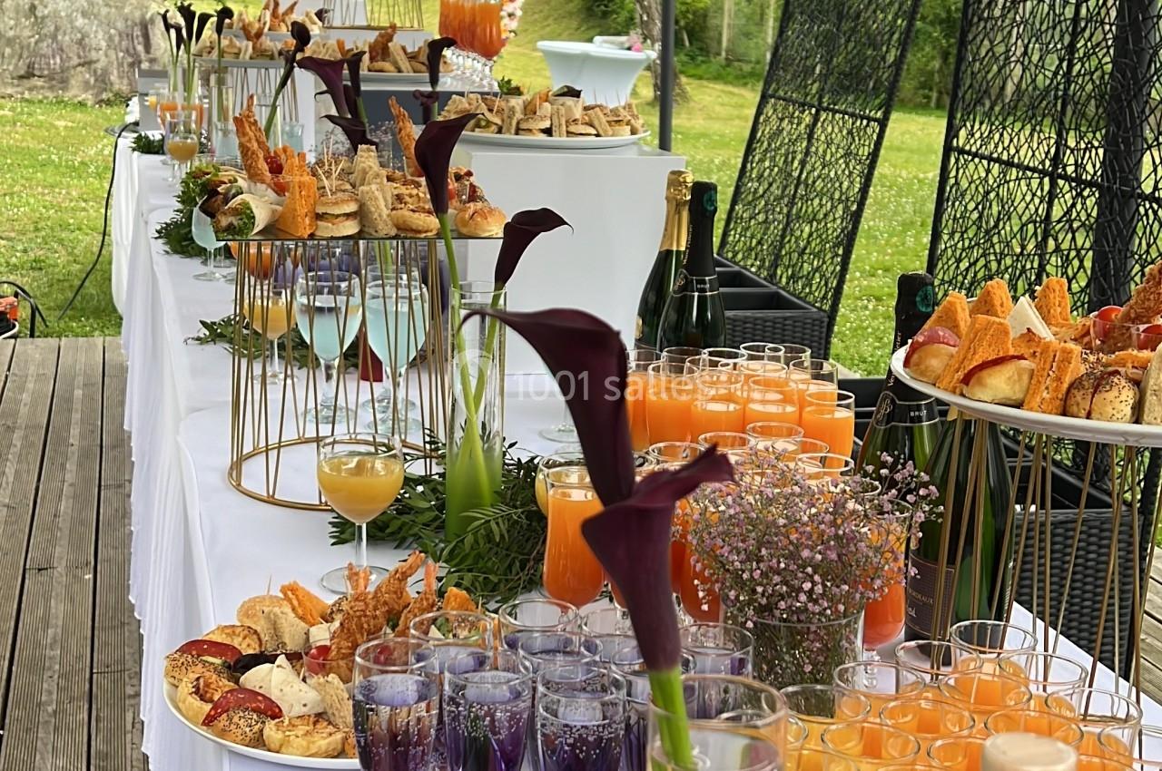 Buffet en plein air avec boissons, viennoiseries, fruits et décorations florales sous une tente blanche.