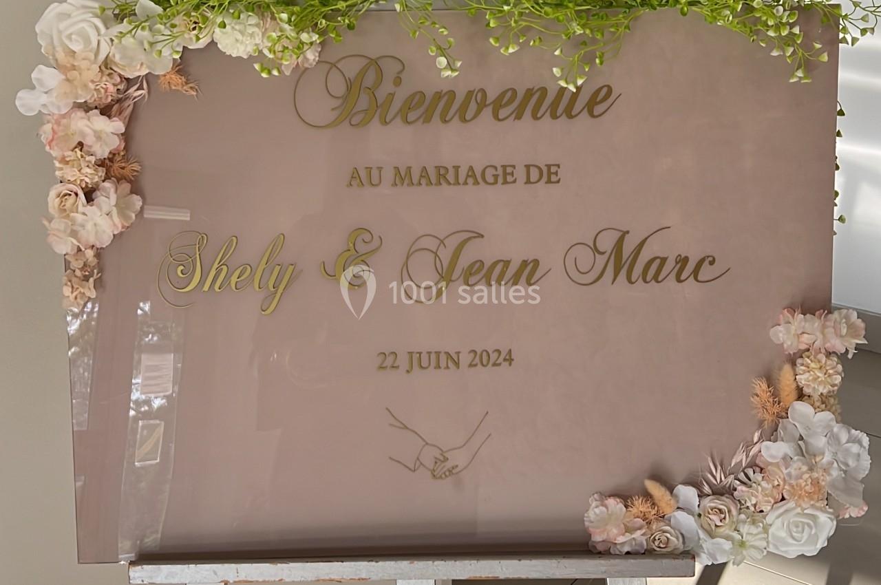 Panneau de bienvenue au mariage de Shely et Jean Marc, décoré de fleurs et feuillages, posé sur un chevalet.