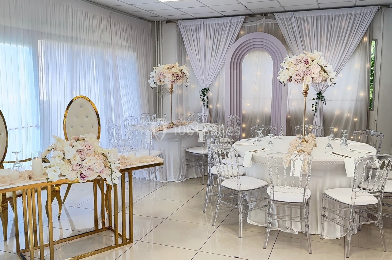 Salle de réception décorée avec des tables rondes, des chaises transparentes et des arrangements floraux élégants.