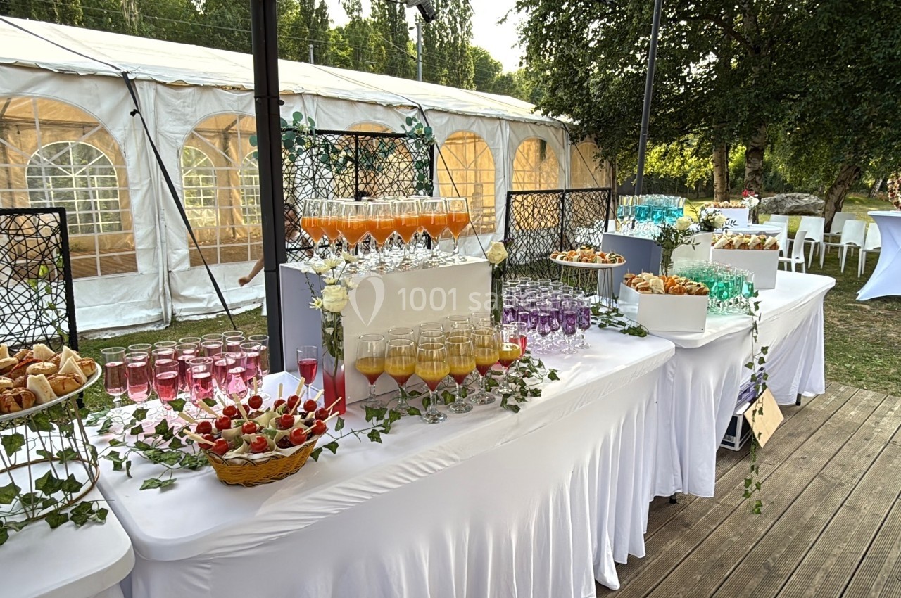 Buffet extérieur avec boissons colorées, verrines et amuse-bouches, installé près d'une tente blanche dans un jardin.