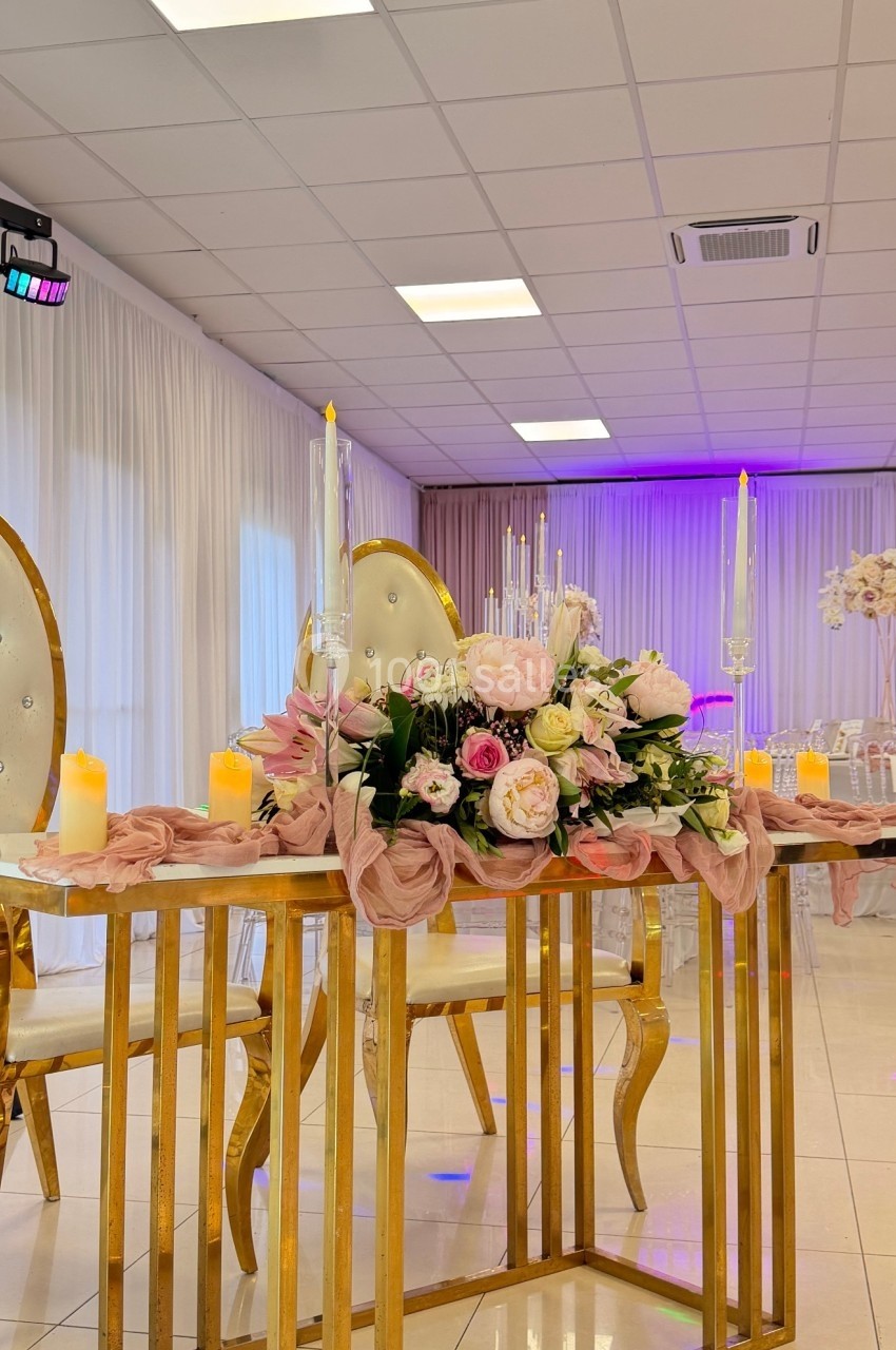 Table décorée avec des fleurs roses et blanches, bougies allumées et chaises élégantes dans une salle lumineuse.