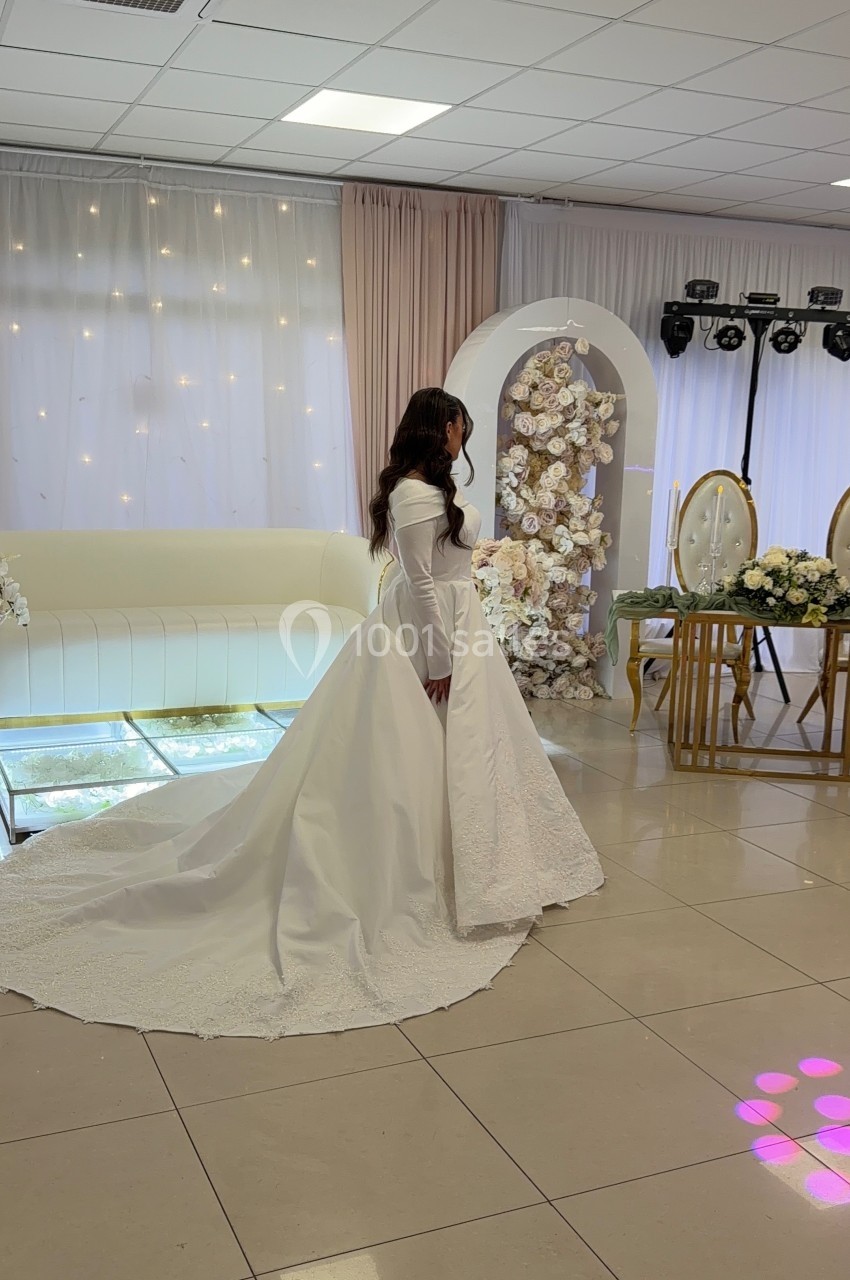Une femme en robe de mariée blanche se tient dans une salle décorée de fleurs et de lumières.