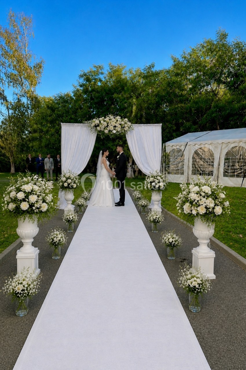 Un couple se tient devant une arche fleurie lors d'une cérémonie de mariage en extérieur, sous un ciel dégagé.