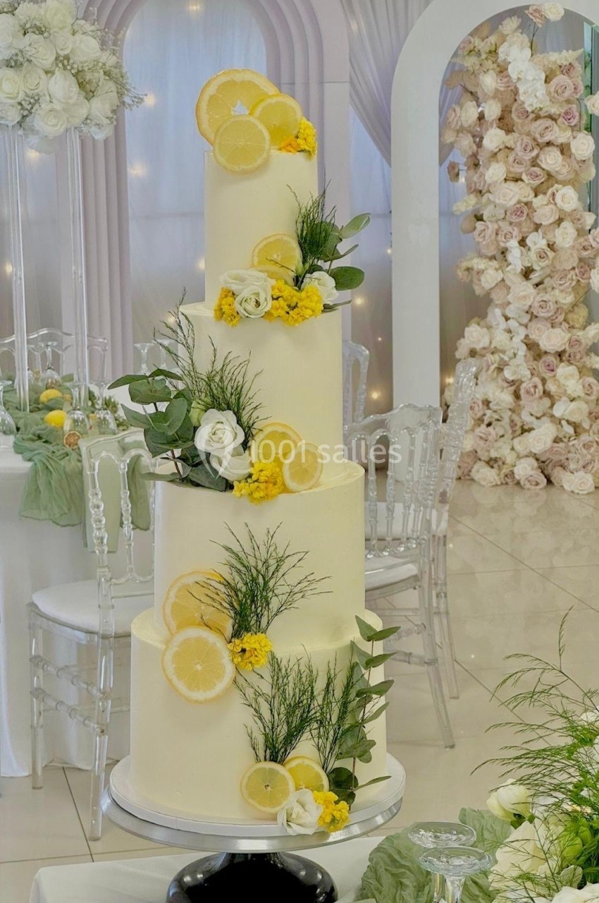 Gâteau de mariage à quatre étages décoré de tranches de citron, fleurs jaunes, blanches et feuillage vert.