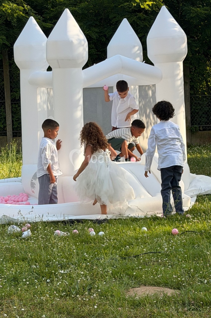 Des enfants jouent autour et à l'intérieur d'un château gonflable blanc dans un jardin verdoyant.