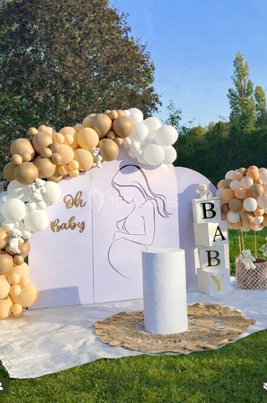 Décoration de baby shower en extérieur avec ballons beige et blanc, cubes ’BABY’ et illustration de femme enceinte.