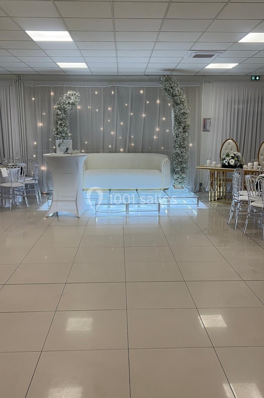 Salle de réception décorée avec un canapé blanc, des arches florales et des tables dressées sur un sol carrelé.