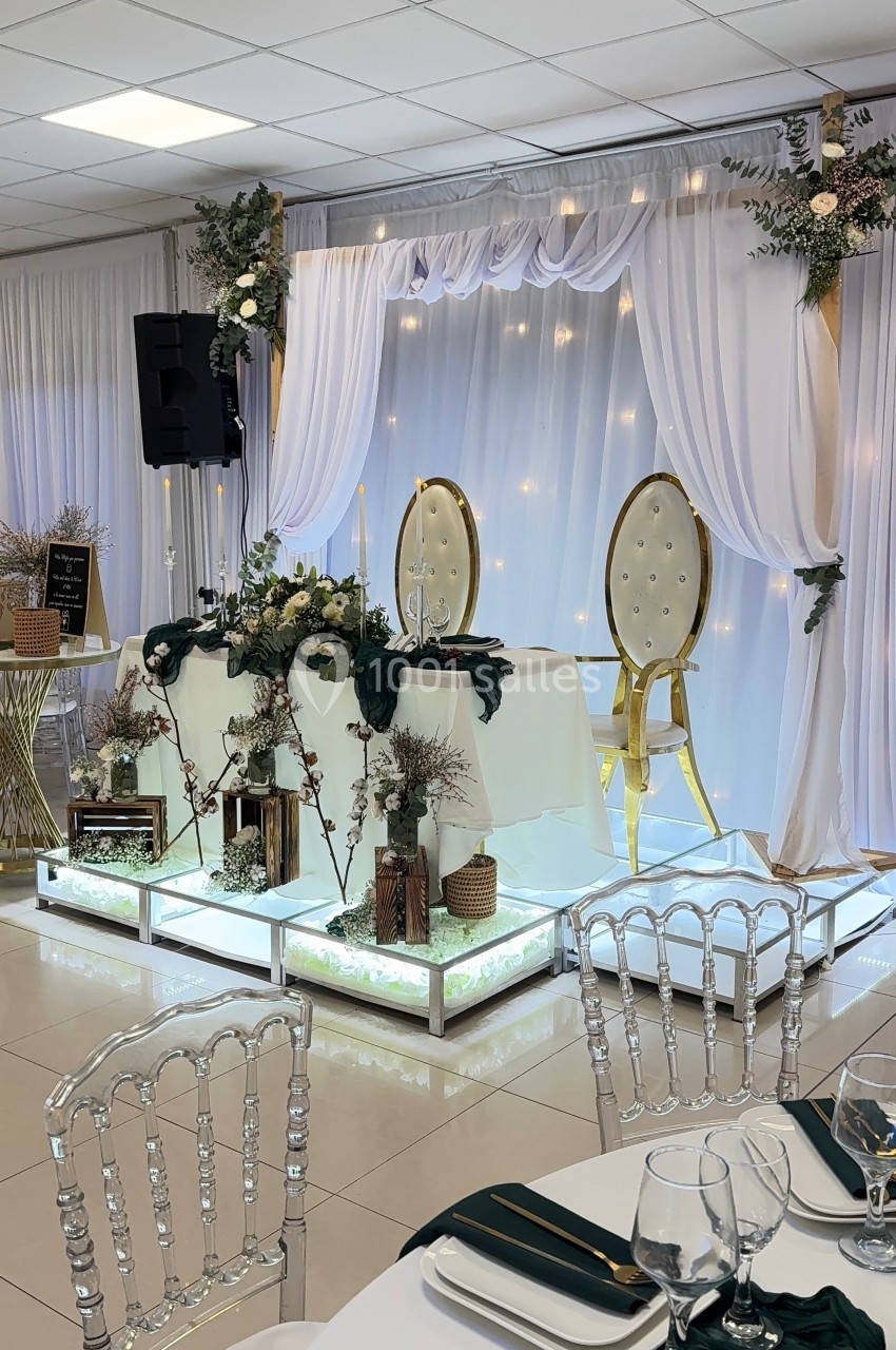 Décoration de table de mariage avec chaises dorées, rideaux blancs, guirlandes lumineuses et détails floraux.