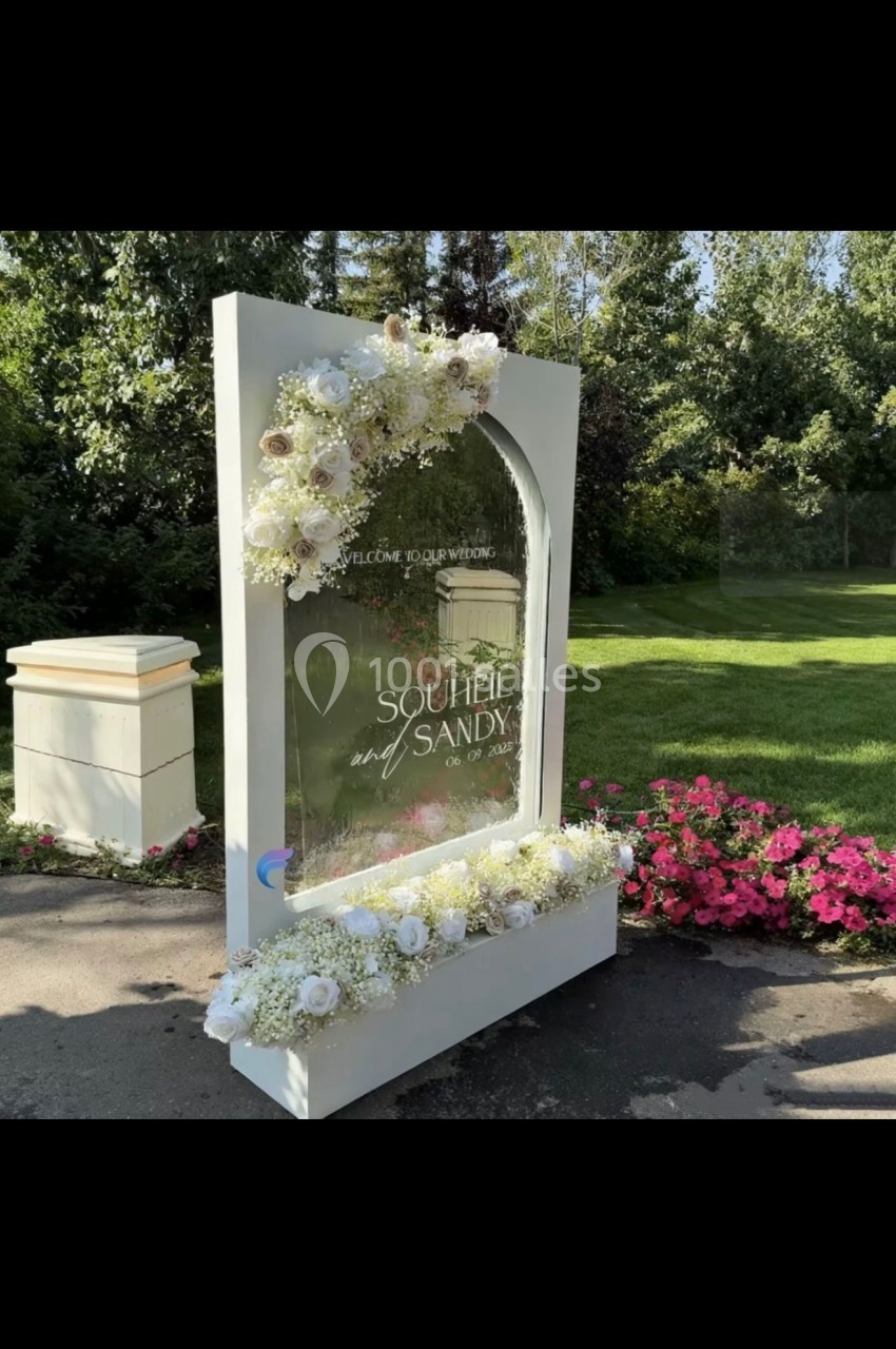 Panneau décoratif en verre entouré de fleurs blanches, installé dans un jardin verdoyant avec des parterres fleuris.