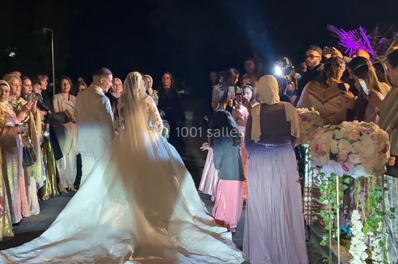 Un couple de mariés avance au milieu d'invités vêtus de tenues traditionnelles lors d'une célébration nocturne.