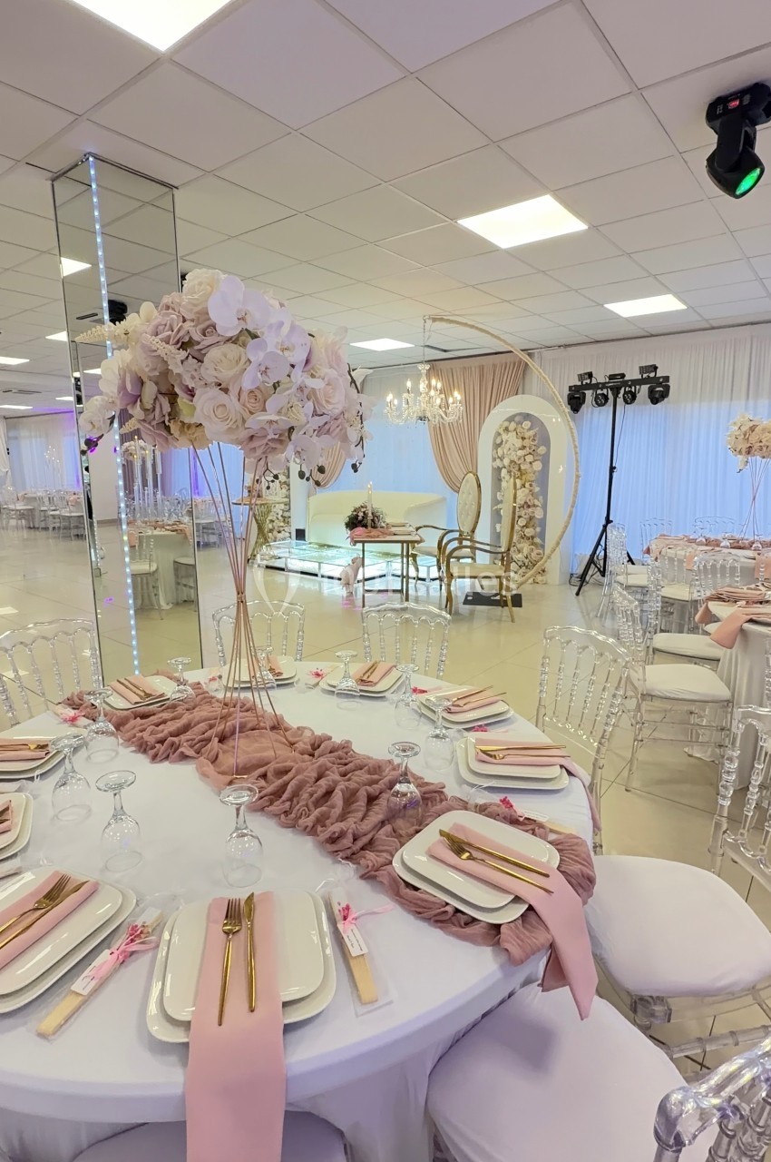 Salle de réception décorée avec des tables élégantes, nappes blanches, serviettes roses et centre de table floral.