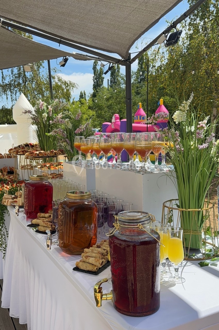 Buffet en extérieur avec boissons, verrines, pâtisseries et décorations florales sous une pergola.