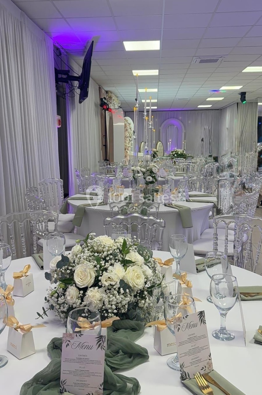 Salle de réception décorée avec des tables élégantes, nappes blanches, bouquets floraux et menus disposés.