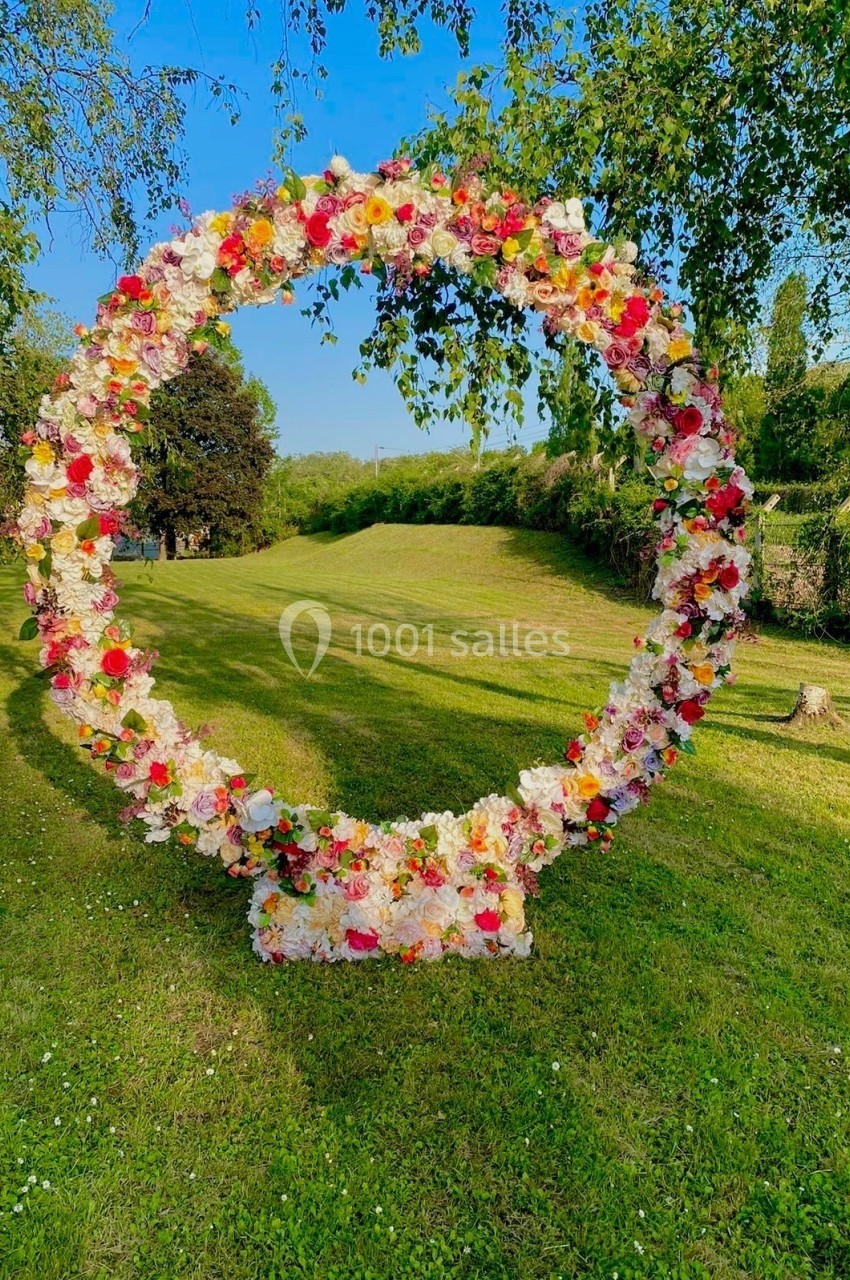 Arche circulaire décorée de fleurs colorées, installée sur une pelouse verdoyante par une journée ensoleillée.