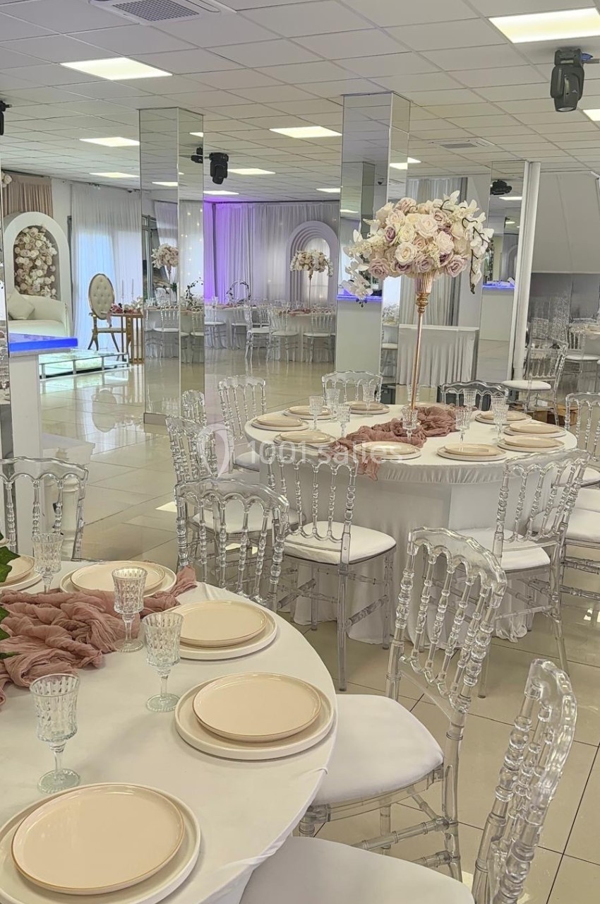 Salle de réception élégante avec tables dressées, chaises transparentes et décoration florale raffinée.