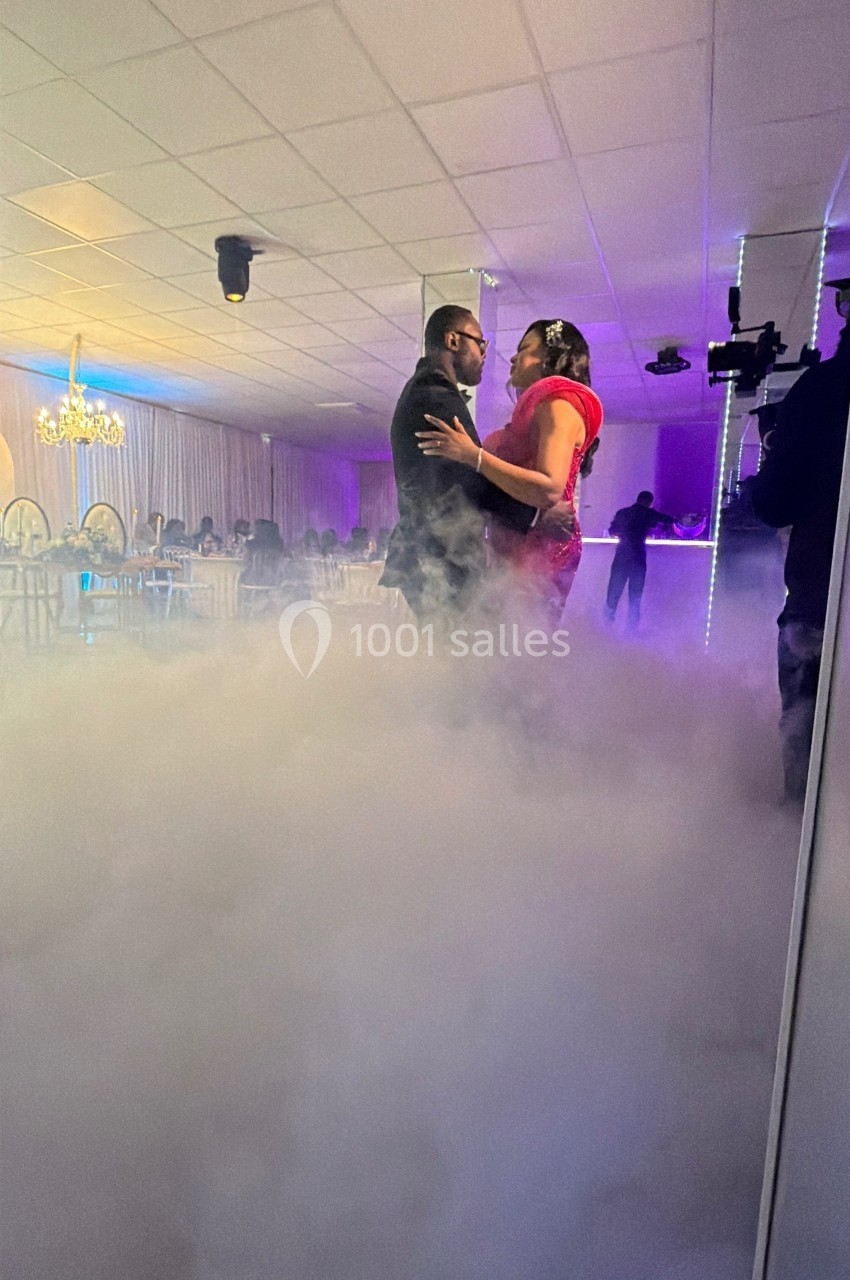 Un couple danse au milieu d'une piste entourée de fumée, dans une salle éclairée par des lumières tamisées.