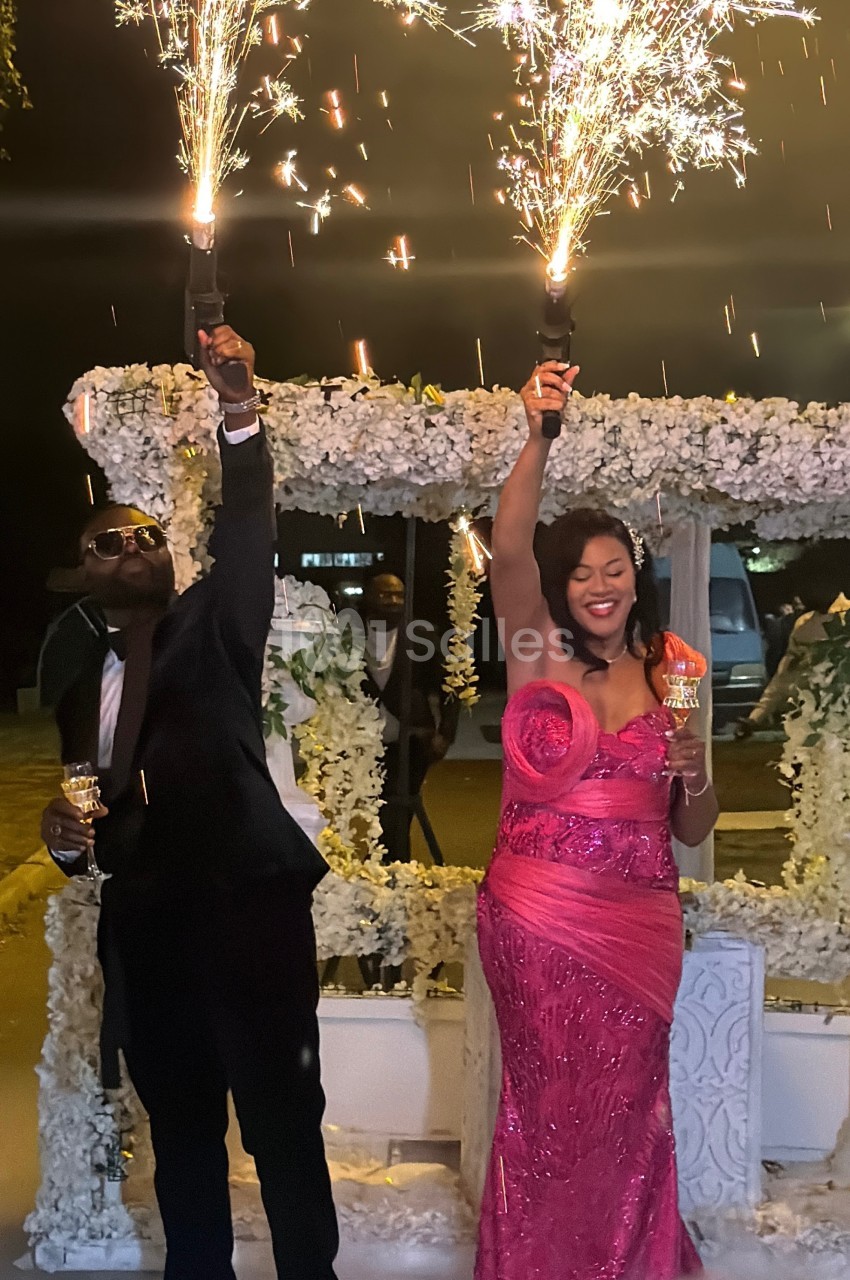Un homme en costume et une femme en robe rose brandissent des cierges magiques allumés lors d'une célébration en soirée.