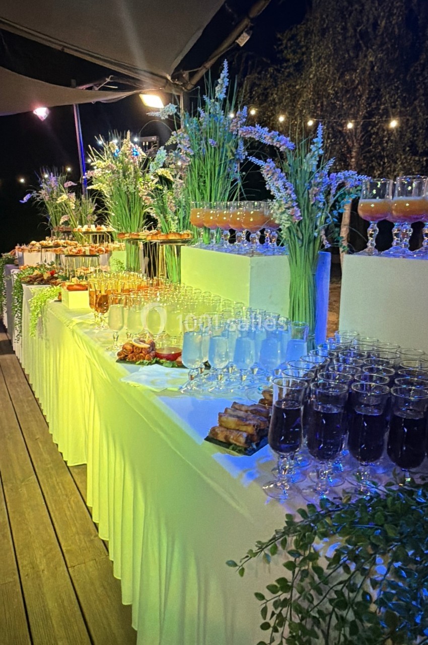 Buffet de boissons et amuse-bouches disposé sur des tables décorées de fleurs, éclairé dans une ambiance nocturne.