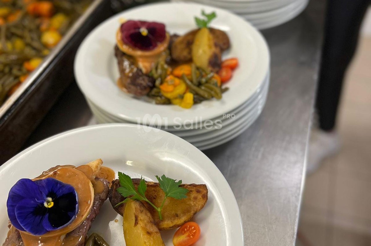 Assiette garnie de viande, légumes verts, pommes de terre, tomates cerises et fleur comestible en décoration.