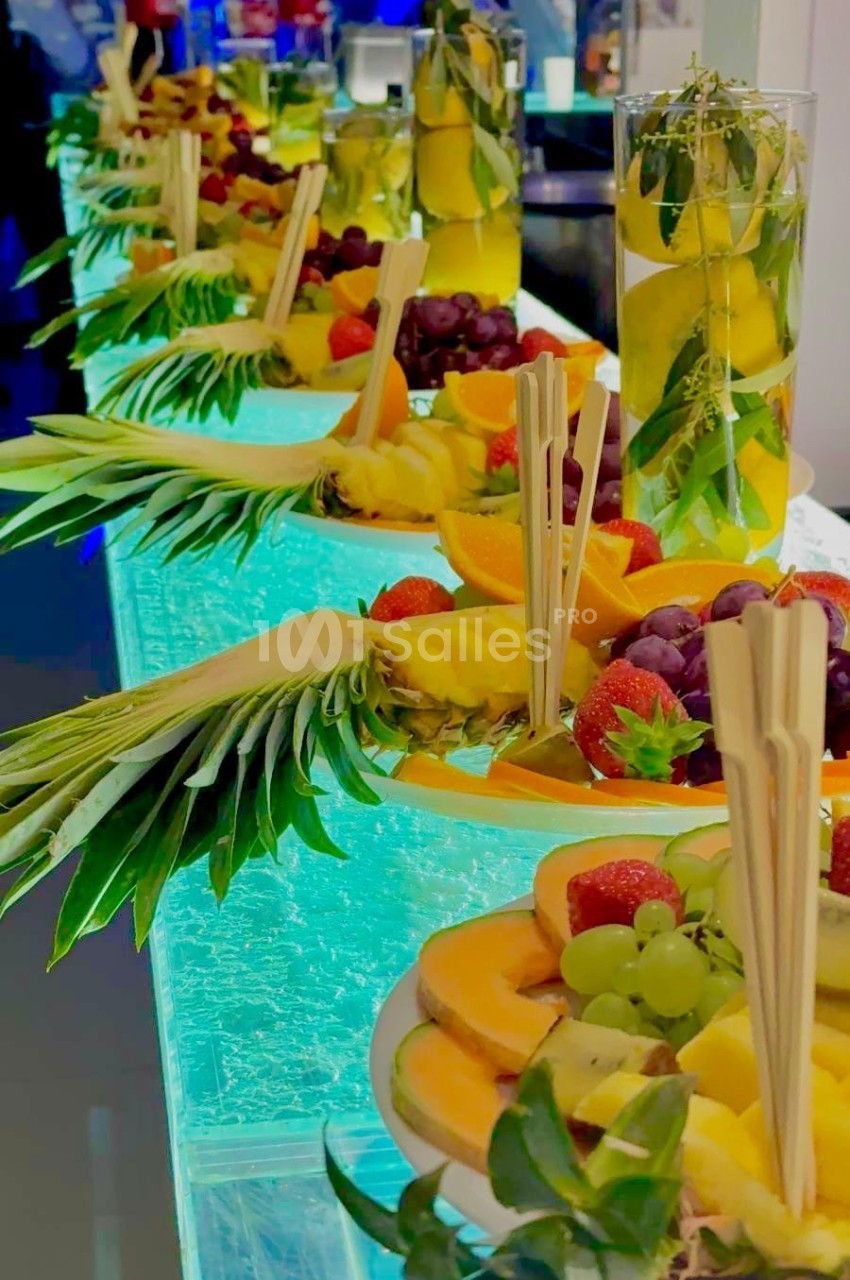 Plateau de fruits frais variés avec ananas, raisins, fraises et oranges, disposés sur une table lumineuse.