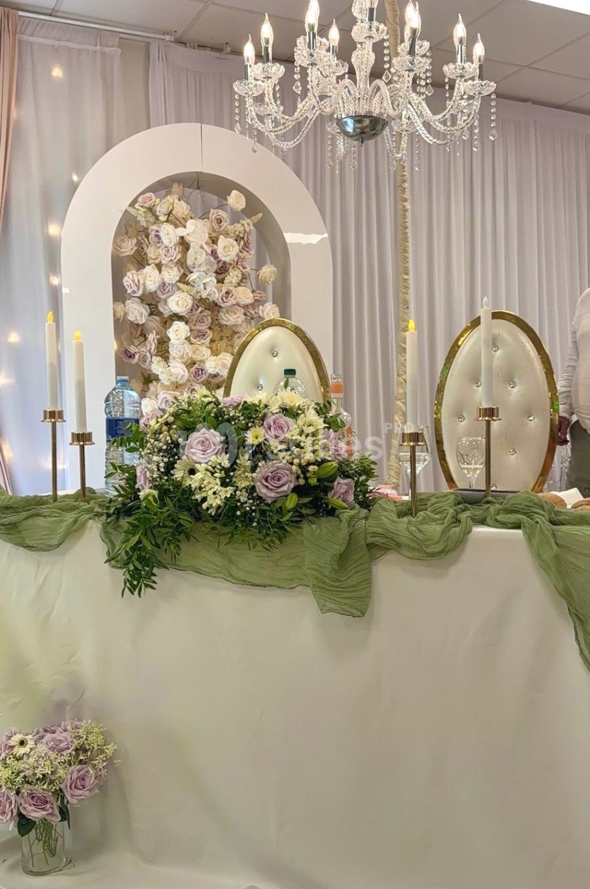 Table décorée pour un événement avec chandeliers, fleurs pastel, nappes blanches et fond orné de roses.