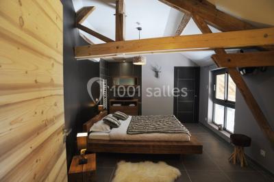 Miniature Location salle Vignieu (Isère) - Domaine de Suzel #4 Chambre avec lit rond, couverture rouge, pétales de rose, lampe de chevet et plafond en bois avec suspension plumeuse.