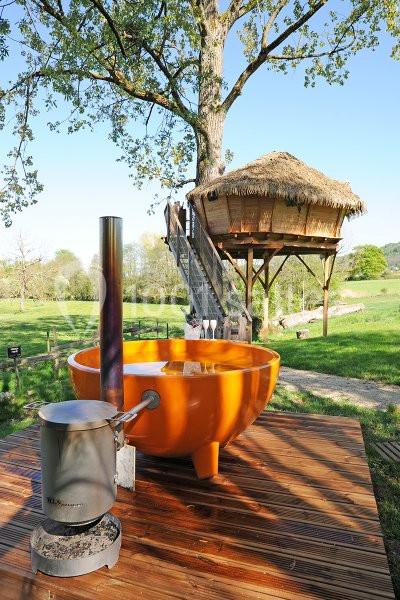 Location salle Vignieu (Isère) - Domaine de Suzel #22 Bain nordique orange sur une terrasse en bois, avec une cabane perchée dans un arbre en arrière-plan.