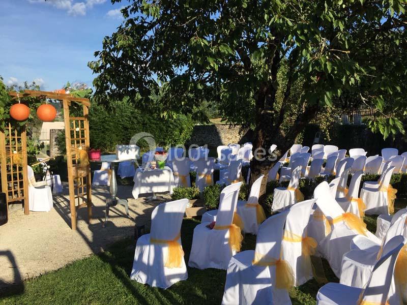 Location salle Vignieu (Isère) - Domaine de Suzel #12 Chaises blanches décorées de rubans orange disposées en extérieur sous un arbre pour une cérémonie.
