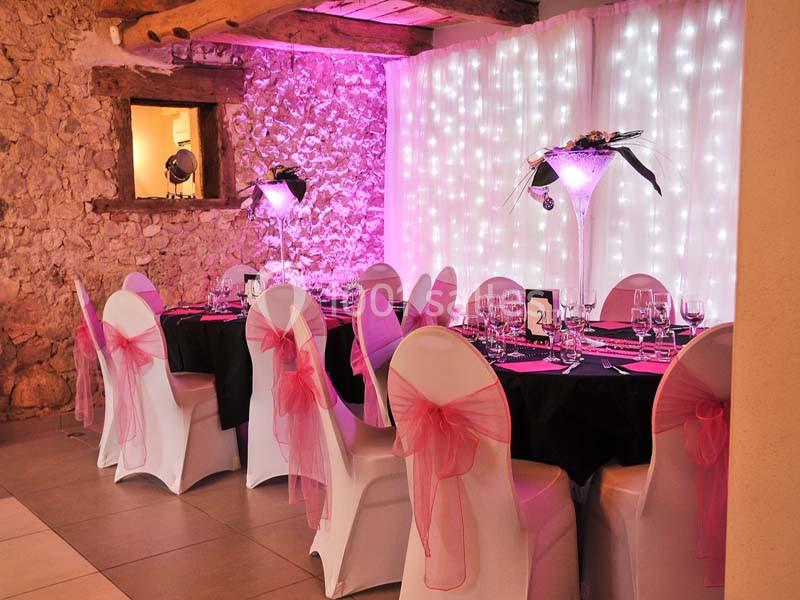 Location salle Vignieu (Isère) - Domaine de Suzel #7 Salle décorée pour un événement avec des tables dressées, des chaises blanches ornées de nœuds roses et un éclairage tamisé.