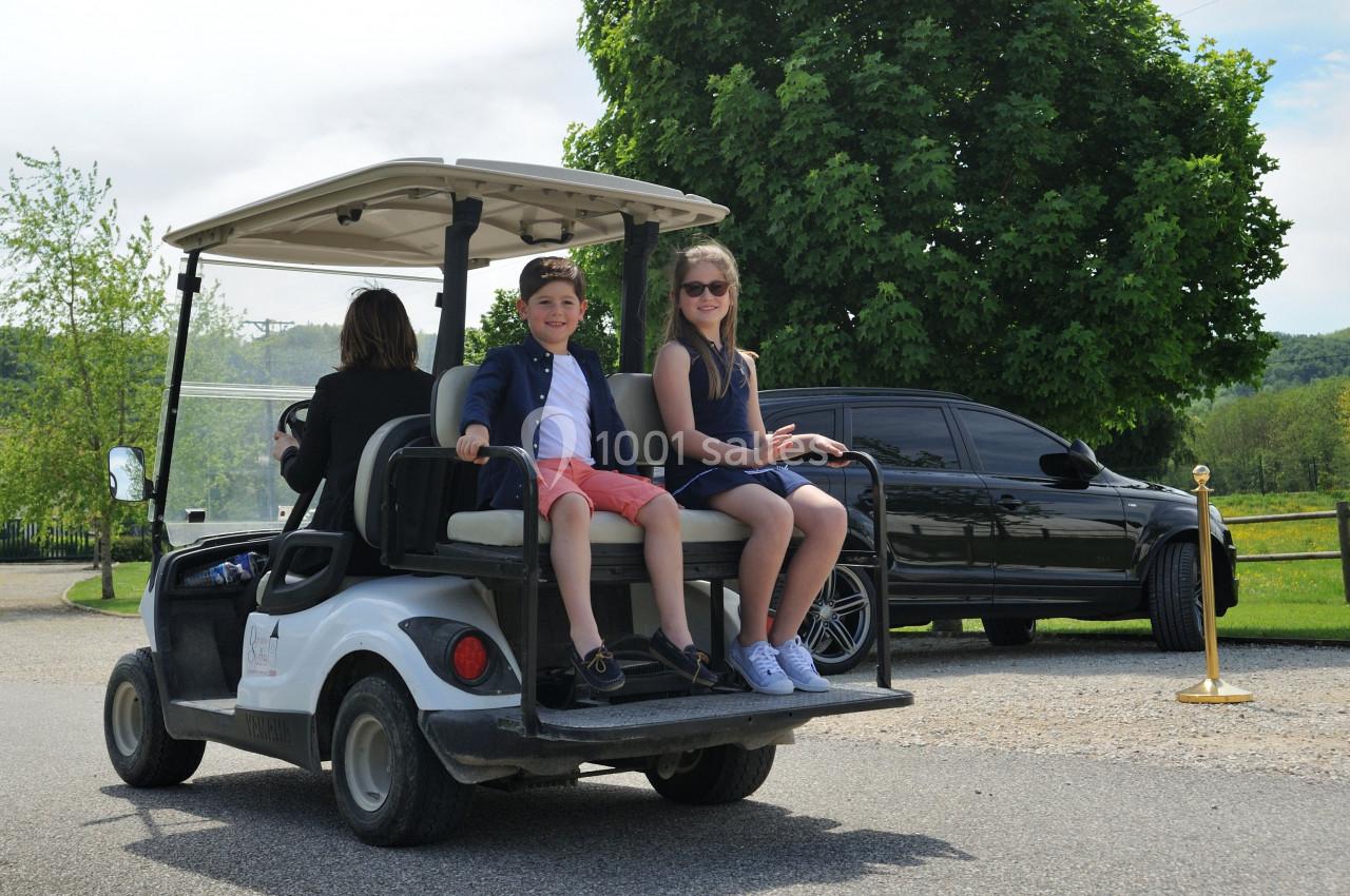 Location salle Vignieu (Isère) - Domaine de Suzel #25 Deux enfants assis à l'arrière d'une voiturette de golf blanche, accompagnés d'un adulte conduisant.
