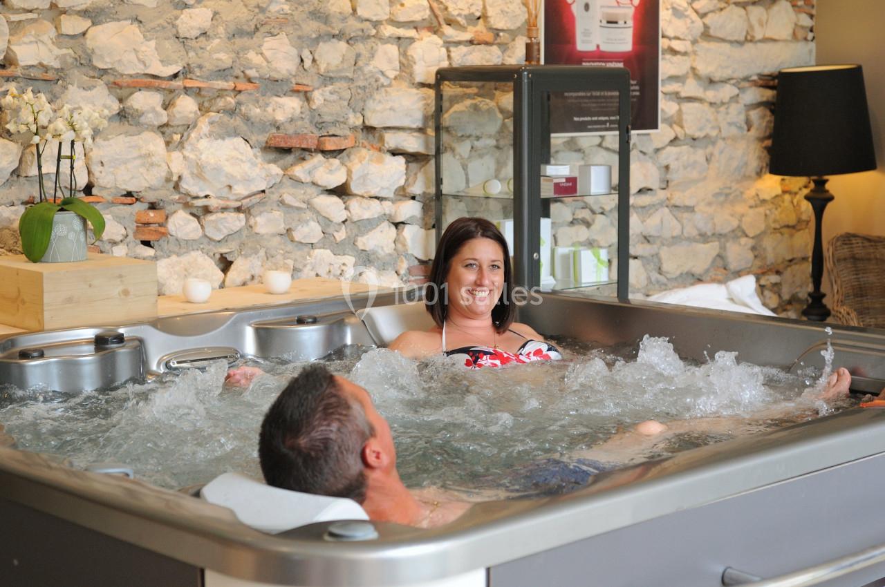 Location salle Vignieu (Isère) - Domaine de Suzel #9 Deux personnes se détendent dans un jacuzzi intérieur, entouré de murs en pierre et d'une décoration chaleureuse.