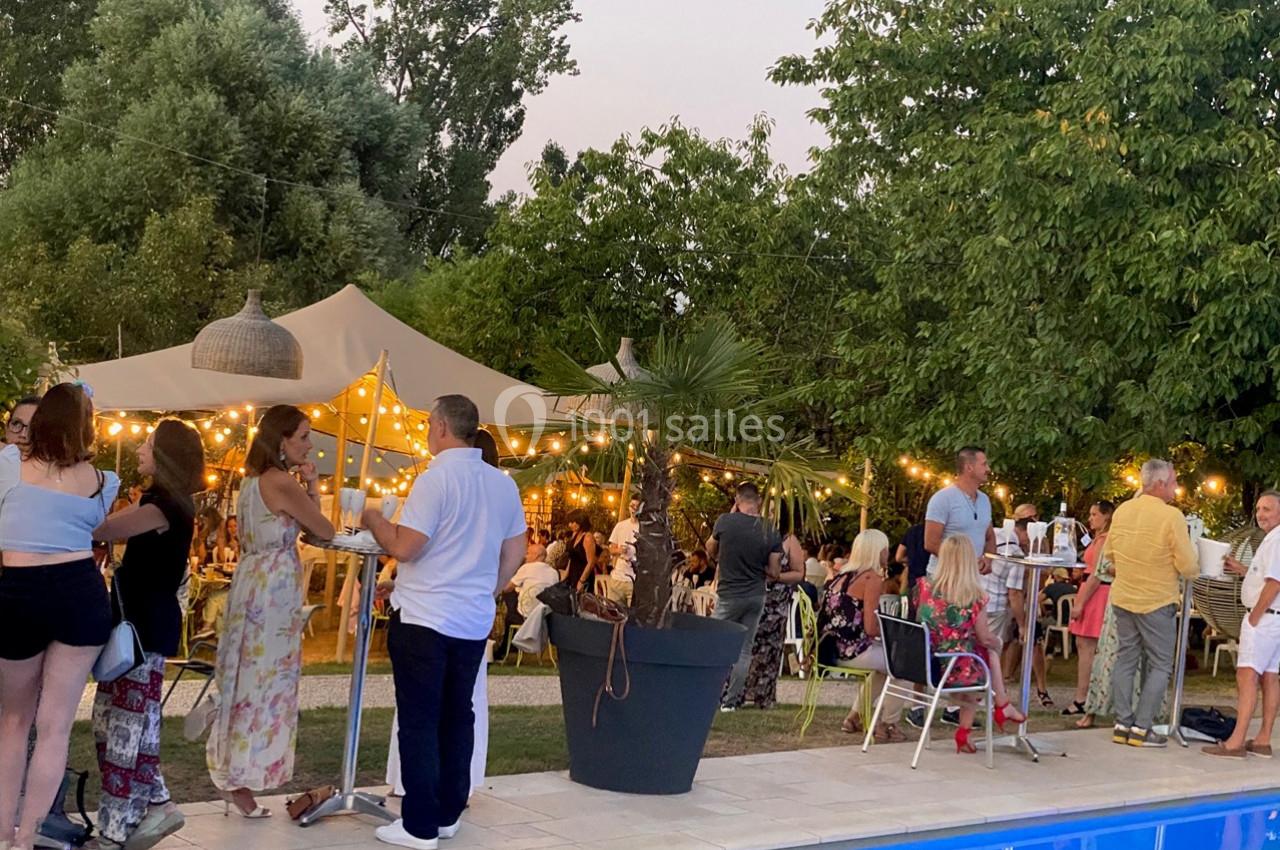 Location salle Vignieu (Isère) - Domaine de Suzel #33 Personnes rassemblées près d'une piscine dans un jardin éclairé par des guirlandes lumineuses, ambiance festive en soirée.