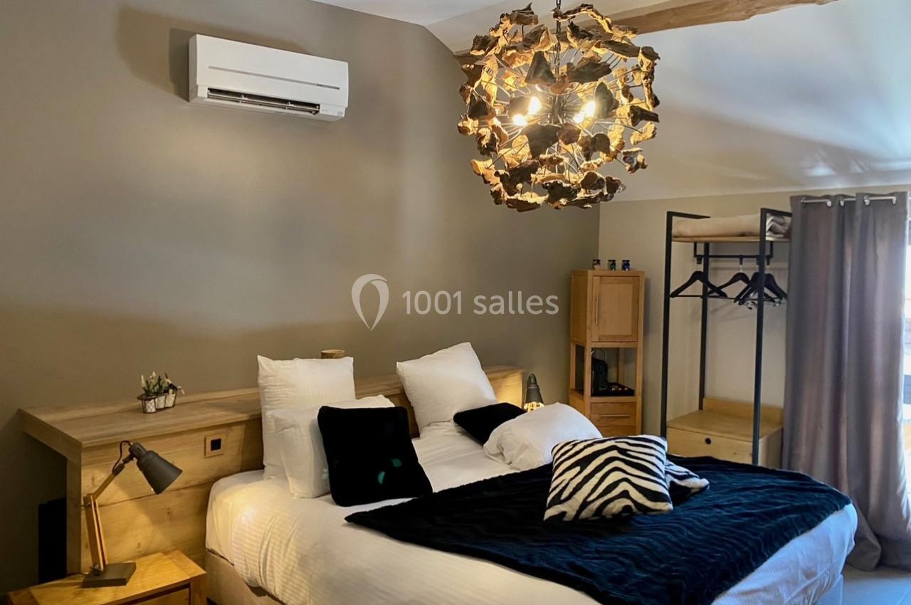 Location salle Vignieu (Isère) - Domaine de Suzel #42 Chambre avec lit double, linge de lit sombre, luminaire en bois, climatisation murale et mobilier en bois clair.