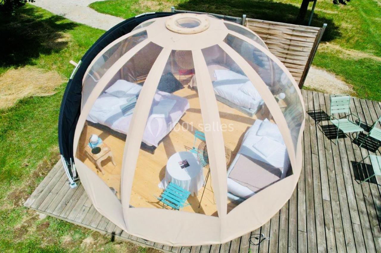 Location salle Vignieu (Isère) - Domaine de Suzel #45 Vue aérienne d'une bulle transparente aménagée avec deux lits, une table et des chaises sur une terrasse en bois.