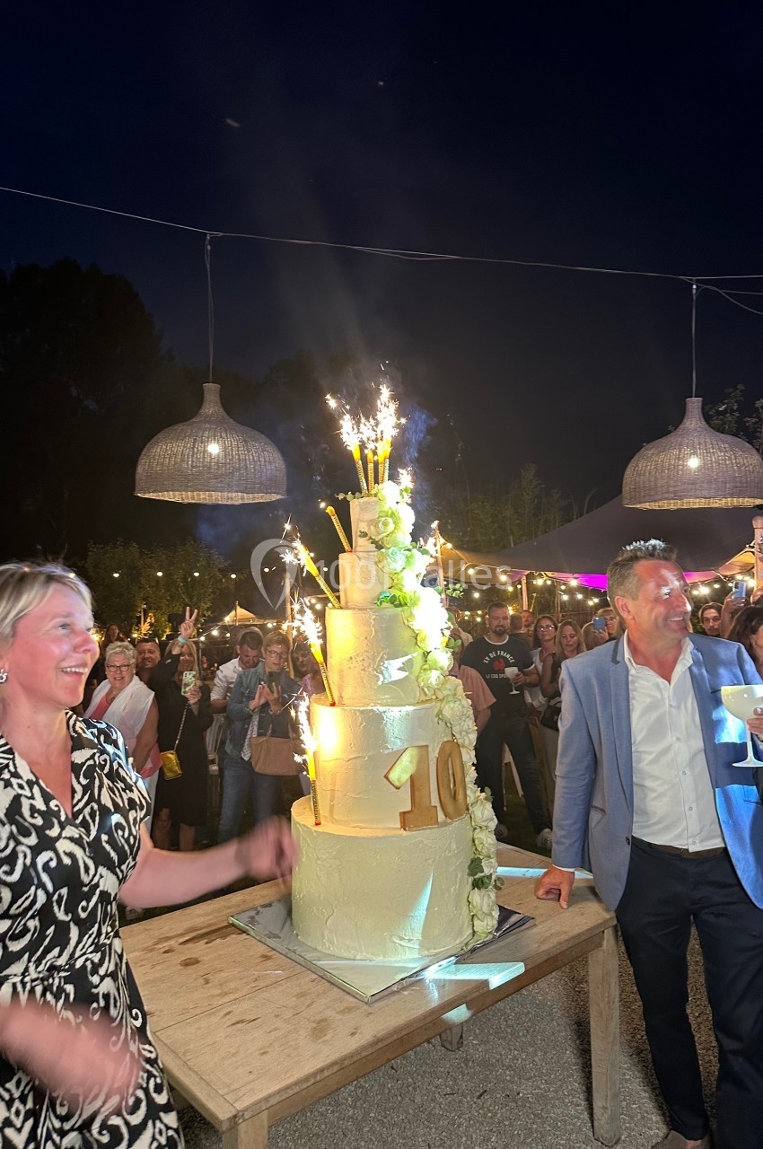 Location salle Vignieu (Isère) - Domaine de Suzel #50 Un gâteau de fête à plusieurs étages avec des bougies étincelantes, entouré de personnes célébrant en extérieur.