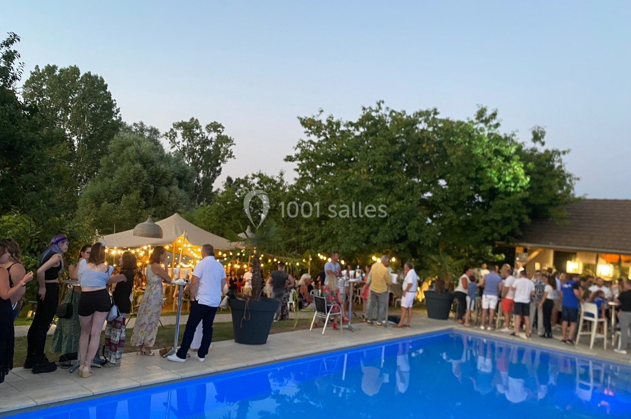 Location salle Vignieu (Isère) - Domaine de Suzel #52 Groupe de personnes rassemblées près d'une piscine au crépuscule, avec guirlandes lumineuses et tentes dans un jardin.